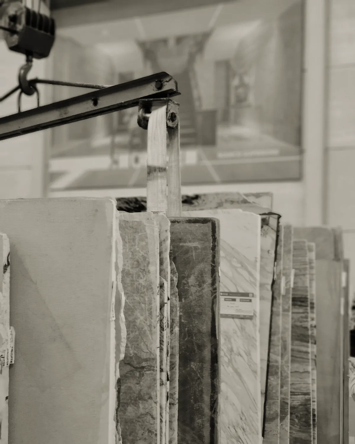 Stone slabs standing in a rack beneath a lifting beam and hook in a fabrication workshop